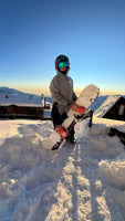 Person holding a snowboard in a snowy landscape with a clear blue sky.